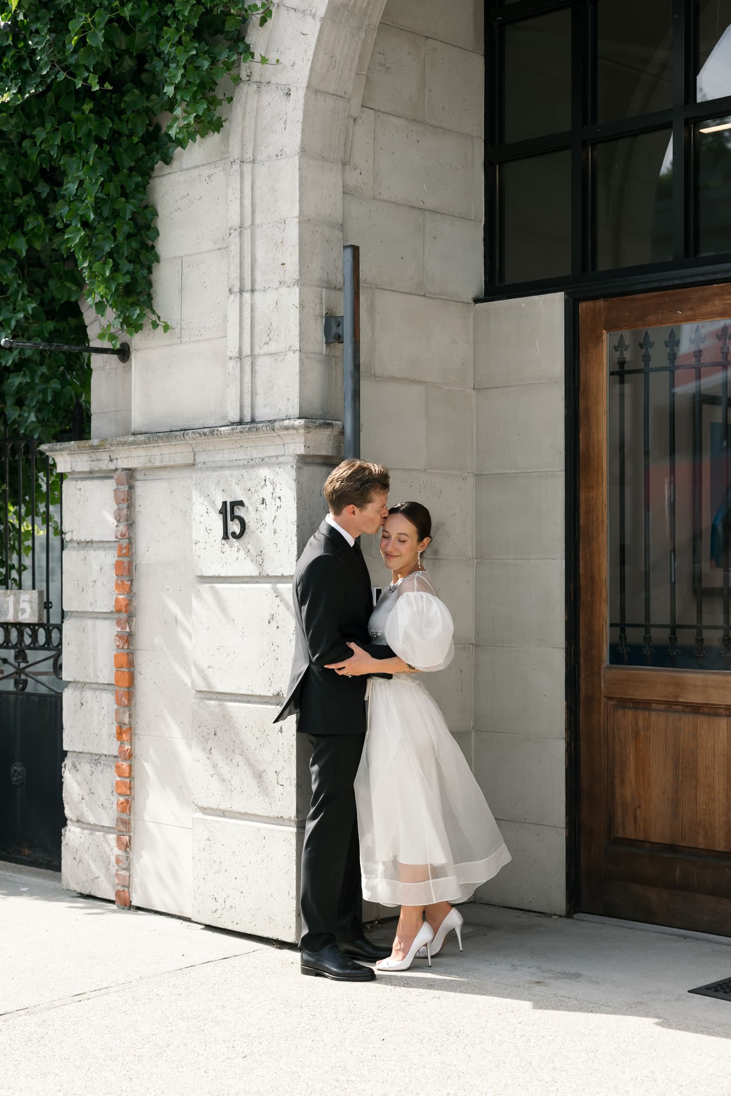 Bride and groom posing together indoors beside a large window.