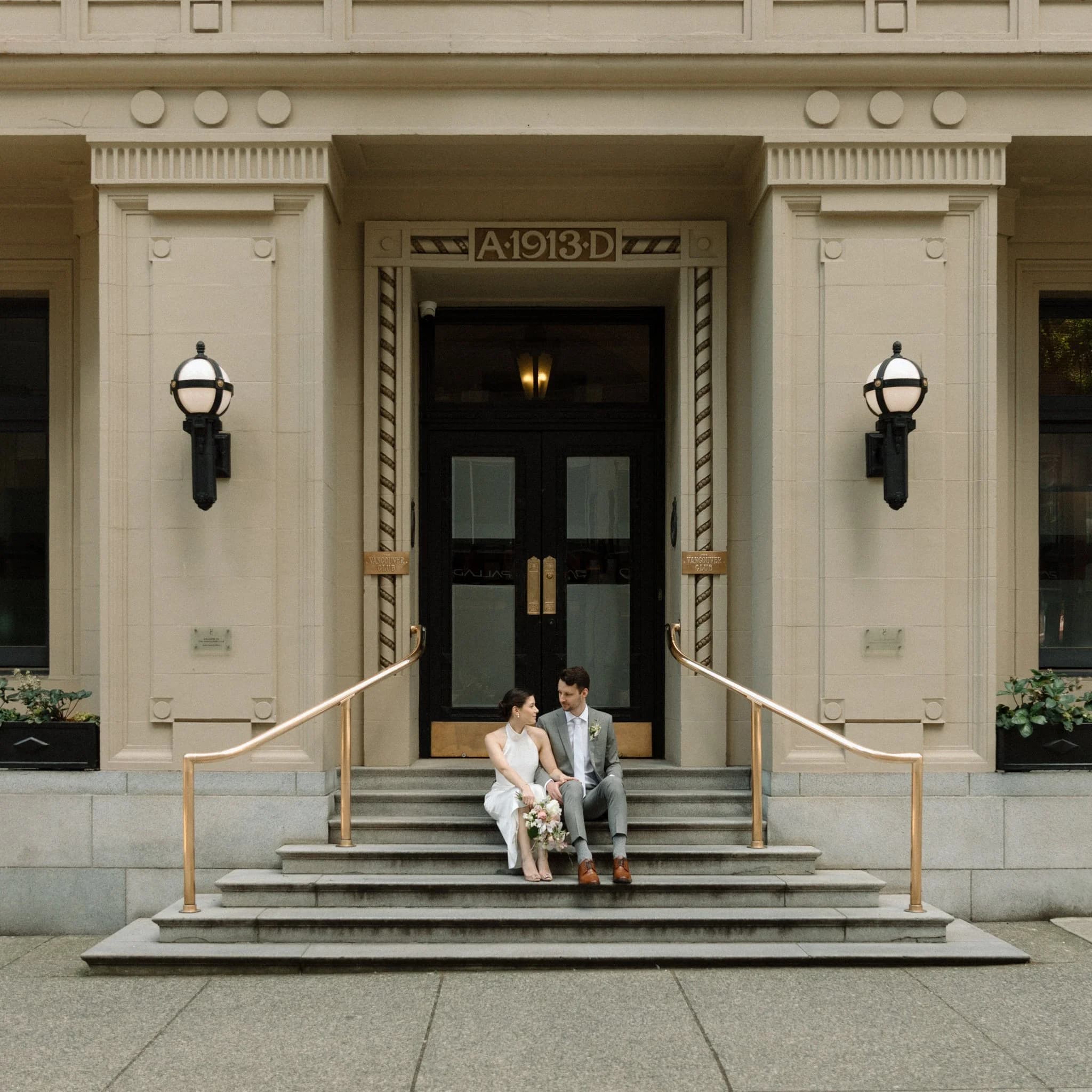 A couple sitting on the steps of a grand entrance, seen from a distance.