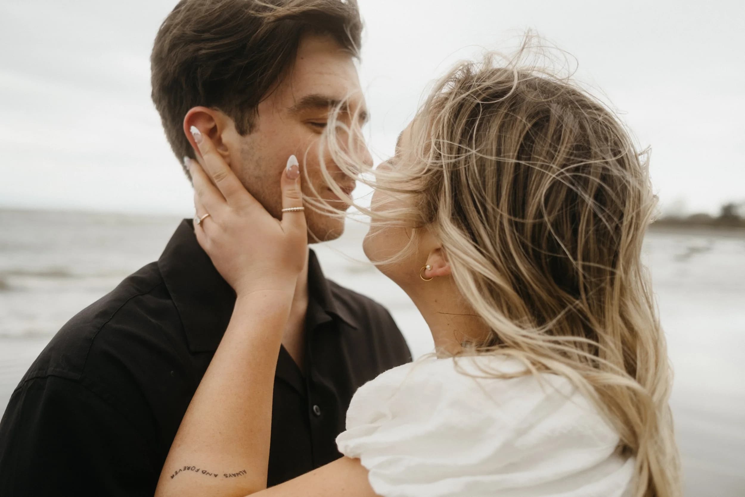 A close, intimate moment between a couple on a windy beach.