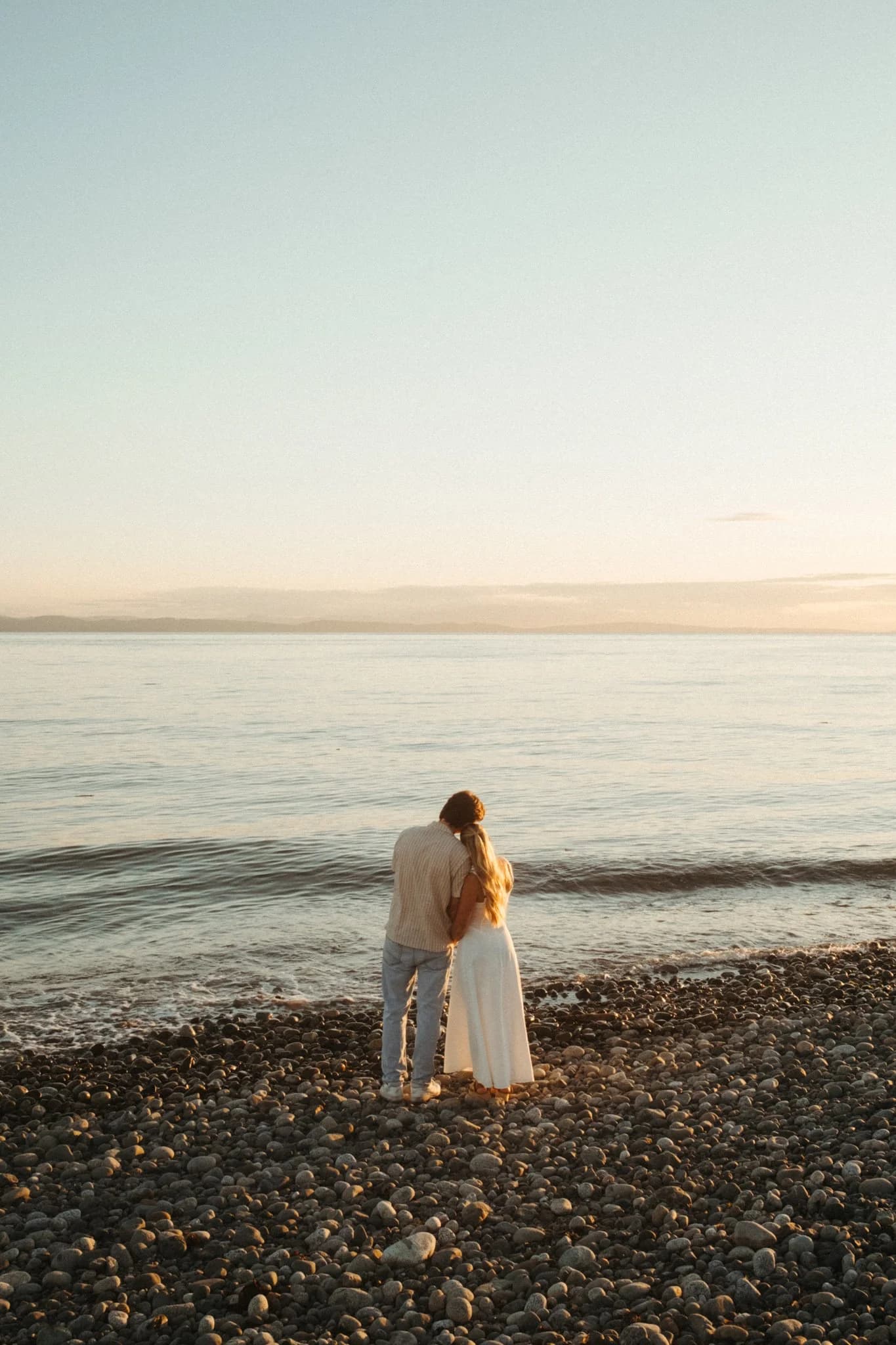 A quiet portrait of a couple on a pebble beach at sunset.