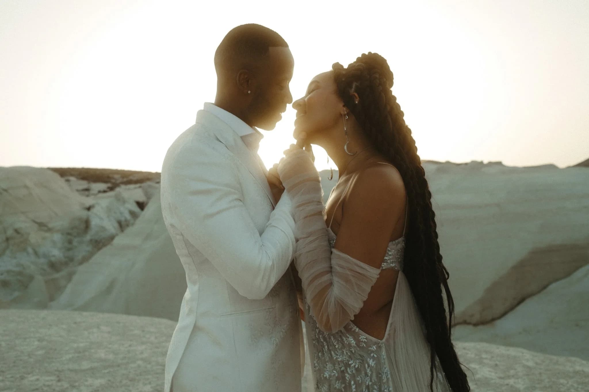 A couple embracing outdoors at sunset in elegant formal outfits.